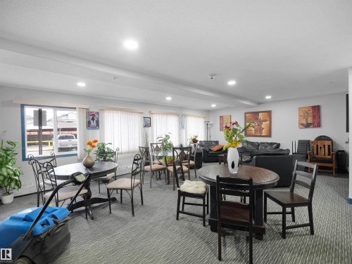 This common area features recessed lighting, carpet flooring, multiple windows with blinds, and various seating arrangements including tables with chairs and couches - 106 2305 35A Avenue Nw, Edmonton, AB - Indoor