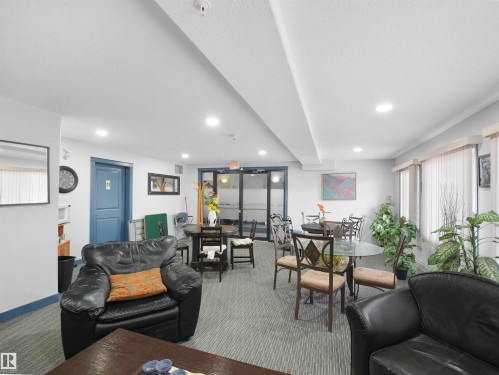 Spacious common area featuring recessed lighting, a blue accent door, and large windows with sheer curtains - 106 2305 35A Avenue Nw, Edmonton, AB - Indoor