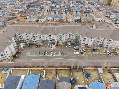 This property features a multi-story building with a light-colored exterior and balconies, surrounded by a paved parking area with marked spaces - 106 2305 35A Avenue Nw, Edmonton, AB - Outdoor With View