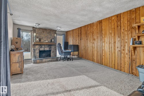 This inviting living space features a stone fireplace with a wooden mantel, a large window providing natural light, and a prominent wood-paneled accent wall - 160068 Twp 531, Rural Lamont County, AB - Indoor With Fireplace