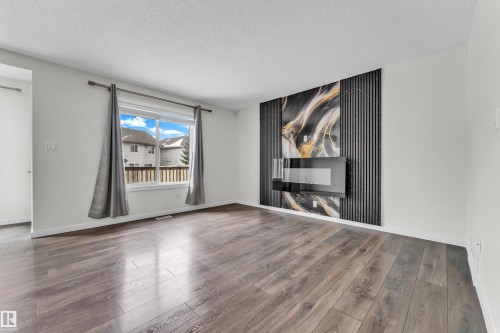 The main living area features hardwood flooring, a large window with grey curtains, and a contemporary wall-mounted fireplace - 4416 6 Street, Edmonton, AB - Indoor Photo Showing Living Room