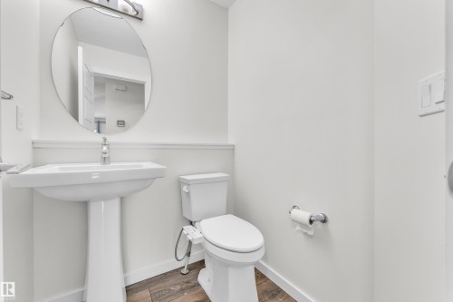 Bathroom featuring a pedestal sink, a toilet, an oval mirror, and dark wood-look flooring - 4416 6 Street, Edmonton, AB - Indoor Photo Showing Bathroom