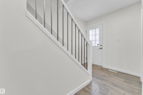 Entryway featuring wood-look flooring, a white door with frosted glass, and a staircase with white railings and dark balusters - 4416 6 Street, Edmonton, AB - Indoor Photo Showing Other Room