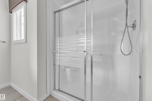 The bathroom features a shower with sliding glass doors, a showerhead with a handheld sprayer, and a window with a valance - 4416 6 Street, Edmonton, AB - Indoor Photo Showing Bathroom