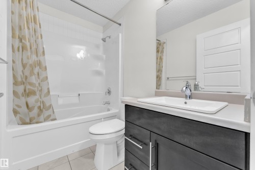 Bathroom featuring a white bathtub and shower unit, a dark wood vanity with a white countertop and rectangular sink, and tile flooring - 4416 6 Street, Edmonton, AB - Indoor Photo Showing Bathroom