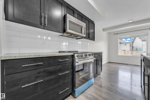 The kitchen features dark cabinetry, light countertops, a stainless steel microwave and range, and subway tile backsplash - 4416 6 Street, Edmonton, AB - Indoor Photo Showing Kitchen With Upgraded Kitchen