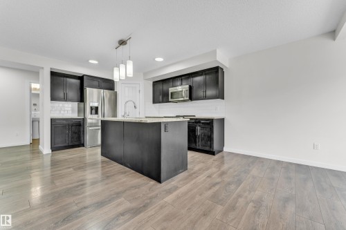 The kitchen features dark cabinetry, a kitchen island with a light-colored countertop, and stainless steel appliances - 4416 6 Street, Edmonton, AB - Indoor Photo Showing Kitchen With Upgraded Kitchen