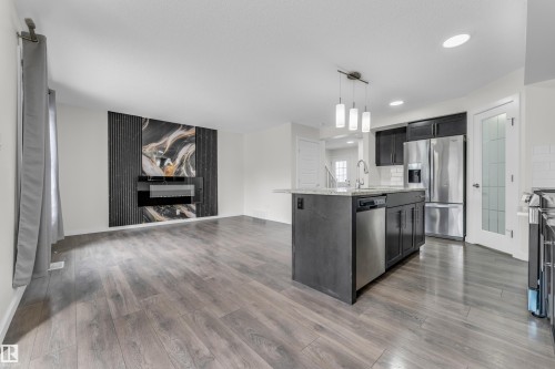 This open-concept living area features wood-look flooring, a modern fireplace with a decorative accent wall, and a kitchen island with a sink and pendant lighting - 4416 6 Street, Edmonton, AB - Indoor Photo Showing Kitchen With Stainless Steel Kitchen With Upgraded Kitchen