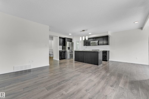 Spacious open concept kitchen and living area featuring hardwood flooring, dark cabinetry, stainless steel appliances, and a kitchen island with pendant lighting - 4416 6 Street, Edmonton, AB - Indoor Photo Showing Kitchen