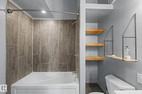 Bathroom featuring a white bathtub, gray tiled shower surround, and built-in wooden shelves - 5920 132 Avenue, Edmonton, AB - Indoor Photo Showing Bathroom