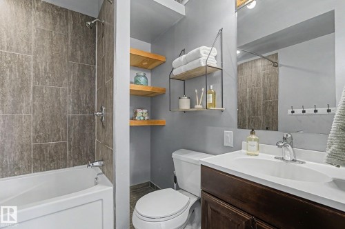 Well-appointed bathroom featuring a bathtub with a tiled shower surround, a toilet, a vanity with a white sink, and decorative shelving - 5920 132 Avenue, Edmonton, AB - Indoor Photo Showing Bathroom
