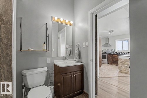 This restroom features a white toilet, a vanity with a dark wood cabinet and white countertop, and a mirror with overhead lighting - 5920 132 Avenue, Edmonton, AB - Indoor Photo Showing Bathroom