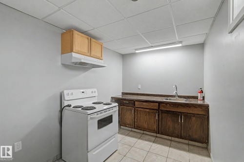 This kitchen area features a white electric stove, wooden upper and lower cabinetry, a sink with a faucet, and tiled flooring - 5920 132 Avenue, Edmonton, AB - Indoor