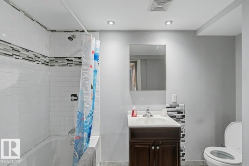 Bathroom featuring a shower and tub combination with subway tile, a vanity with a white countertop and dark wood cabinetry, and a toilet - 5920 132 Avenue, Edmonton, AB - Indoor Photo Showing Bathroom