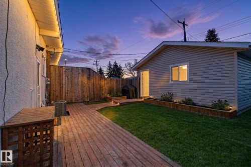 The property features a private yard with a wooden deck, a maintained lawn, and a wooden privacy fence - 5920 132 Avenue, Edmonton, AB - Outdoor With Exterior