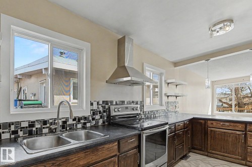 The kitchen features a double basin stainless steel sink with a gooseneck faucet, a mosaic tile backsplash, and dark wood cabinetry - 5920 132 Avenue, Edmonton, AB - Indoor Photo Showing Kitchen With Double Sink