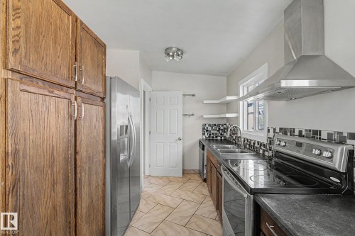 The kitchen features wood cabinetry, a stainless steel refrigerator, and a stainless steel range with a matching range hood - 5920 132 Avenue, Edmonton, AB - Indoor Photo Showing Kitchen With Double Sink