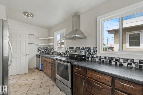 The kitchen features a stainless steel refrigerator, stainless steel range with overhead hood, dark countertops, and a tiled backsplash - 5920 132 Avenue, Edmonton, AB - Indoor Photo Showing Kitchen With Double Sink