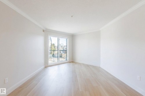 Bright livingroom featuring light-toned flooring, white walls, and a large glass door leading to an east-facting balcony with a black railing - 209 14612 125 Street, Edmonton, AB - Indoor Photo Showing Other Room