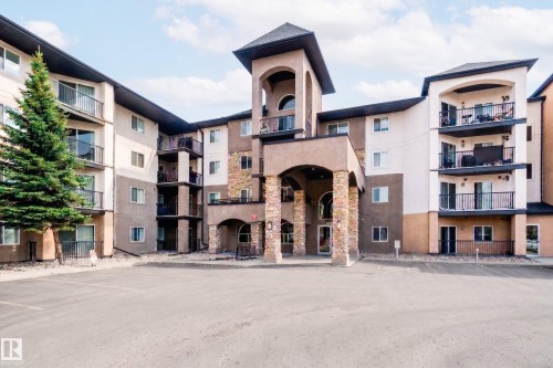 Exterior view of the property, showcasing a multi-story design with balconies, a stone-accented entrance, and a paved parking area - 209 14612 125 Street, Edmonton, AB - Outdoor With Balcony With Facade