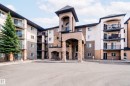 Exterior view of the property, showcasing a multi-story design with balconies, a stone-accented entrance, and a paved parking area - 209 14612 125 Street, Edmonton, AB  - Outdoor With Balcony With Facade 