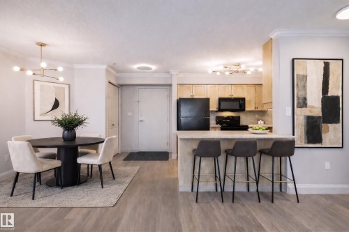 This open concept living area features light wood-style flooring, a dining area with a modern chandelier and seating for four, and a kitchen island with seating for three - 209 14612 125 Street, Edmonton, AB - Indoor