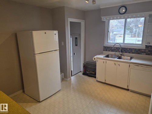 The kitchen features a double basin stainless steel sink, white cabinetry, and a white refrigerator - 3626 111 Avenue, Edmonton, AB - Indoor Photo Showing Kitchen With Double Sink