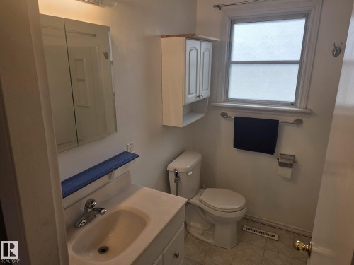 The bathroom features a window with white trim, a toilet, a vanity with an integrated sink and chrome faucet, and a wall-mounted medicine cabinet - 3626 111 Avenue, Edmonton, AB - Indoor Photo Showing Bathroom