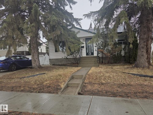 The property features a white exterior with dark trim, a front yard with mature trees, and a concrete pathway leading to the entrance - 3626 111 Avenue, Edmonton, AB - Outdoor