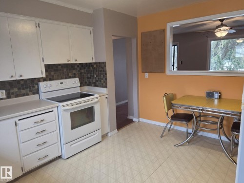 The kitchen features white cabinetry, a white electric range, and a tiled backsplash - 3626 111 Avenue, Edmonton, AB - Indoor Photo Showing Kitchen