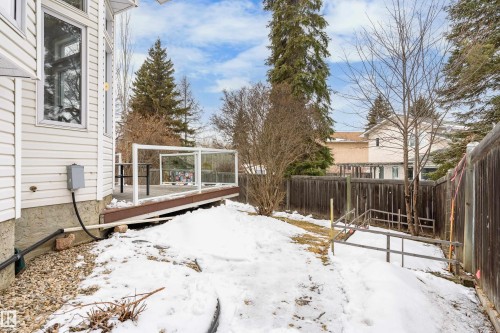The property features a wood deck with glass panel railings, a fenced yard, and established evergreen trees - 10 Harmony Place, St. Albert, AB - Outdoor With Deck Patio Veranda