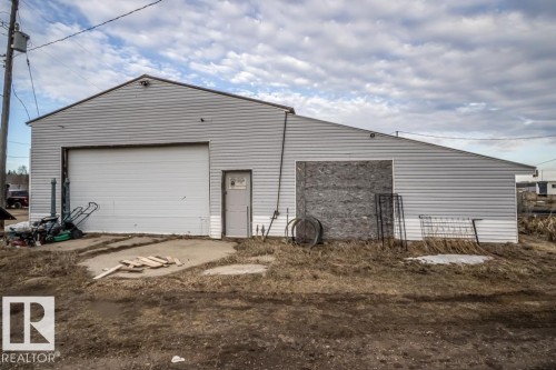Utility building featuring light gray siding, a large white roll-up door, a standard entry door, and a partially enclosed section with plywood - 57027 Sec Hwy 881, Rural St. Paul County, AB 