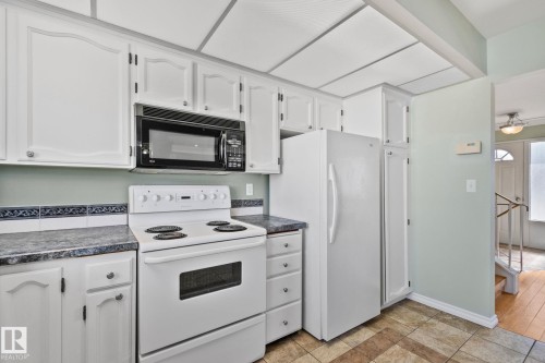 The kitchen features white cabinetry, a white electric range, a black microwave, and a white refrigerator - 2016 138 Avenue, Edmonton, AB - Indoor Photo Showing Kitchen