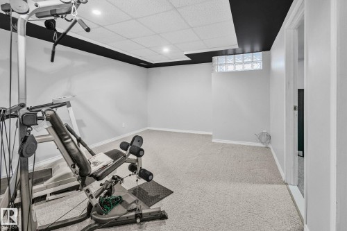 This versatile space features light-colored carpeting, a drop ceiling with recessed lighting, and a glass block window providing natural light - 2016 138 Avenue, Edmonton, AB - Indoor Photo Showing Gym Room