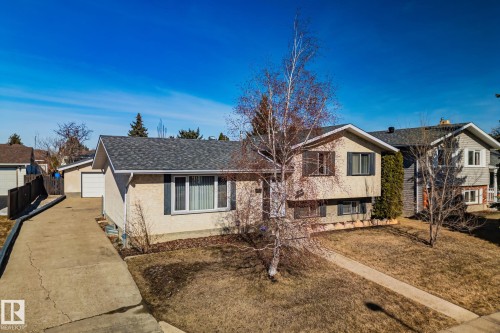 The property features a concrete driveway leading to a garage, a front lawn, and a light-colored exterior with dark window shutters - 2016 138 Avenue, Edmonton, AB - Outdoor