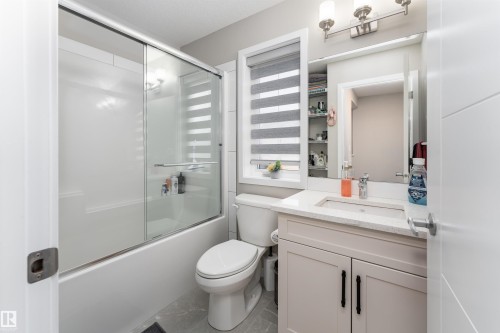 This bathroom features a shower-tub combination with a sliding glass door, a vanity with a light-colored countertop and a sink, and a wall-mounted mirror - 22742 95A Ave, Edmonton, AB - Indoor Photo Showing Bathroom