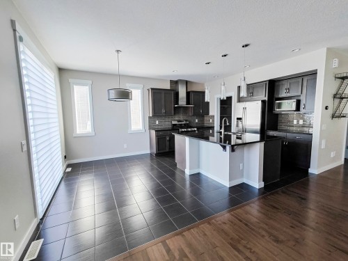 The open concept kitchen features dark cabinetry, stainless steel appliances, a kitchen island with a sink and pendant lighting, and dark tile flooring - 8008 18 Avenue Sw, Edmonton, AB - Indoor Photo Showing Kitchen With Upgraded Kitchen