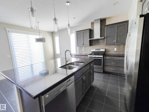 The kitchen features dark grey cabinetry, a stainless steel range with a matching range hood, and a dark tile backsplash - 8008 18 Avenue Sw, Edmonton, AB - Indoor Photo Showing Kitchen With Double Sink With Upgraded Kitchen