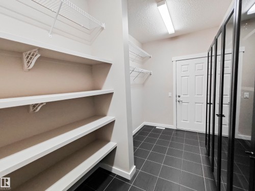 This utility room features dark tiled flooring, a white door, and white painted walls - 8008 18 Avenue Sw, Edmonton, AB - Indoor With Storage