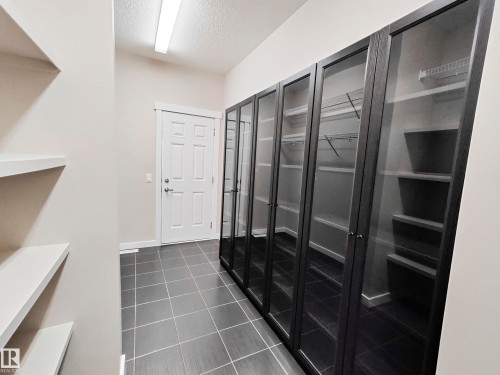 The interior hallway features dark grey tiled flooring, a white door, and extensive built-in storage with glass-fronted doors and shelving - 8008 18 Avenue Sw, Edmonton, AB - Indoor