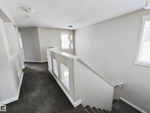 Inviting hallway with neutral painted walls and plush carpeting, featuring a staircase with a white railing and a window providing natural light - 8008 18 Avenue Sw, Edmonton, AB - Indoor Photo Showing Other Room