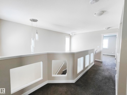 The landing features a contemporary chandelier with three cylindrical lights, a gray carpeted floor, and a white railing with decorative cut-outs - 8008 18 Avenue Sw, Edmonton, AB - Indoor Photo Showing Other Room