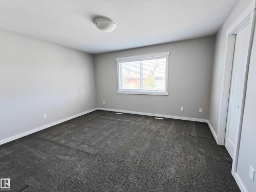 This room features neutral-toned walls, dark gray carpet, a window with blinds, and white trim - 8008 18 Avenue Sw, Edmonton, AB - Indoor Photo Showing Other Room