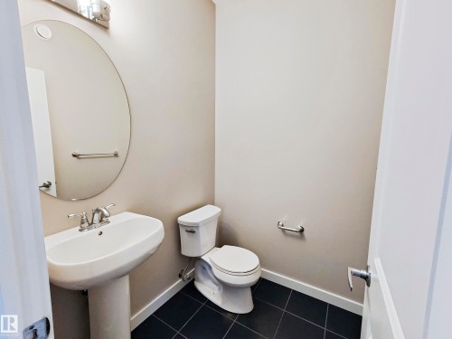 This bathroom features a pedestal sink with a contemporary faucet, a round mirror, and dark tile flooring - 8008 18 Avenue Sw, Edmonton, AB - Indoor Photo Showing Bathroom