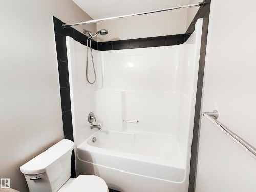 Bathroom featuring a white shower and bathtub combination with a dark tiled surround, and a chrome shower head and faucet - 8008 18 Avenue Sw, Edmonton, AB - Indoor Photo Showing Bathroom