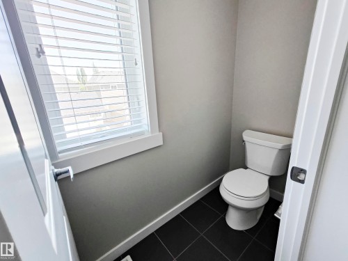 Conveniently located toilet area with a window providing natural light and dark tiled flooring - 8008 18 Avenue Sw, Edmonton, AB - Indoor Photo Showing Bathroom