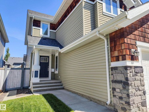 The property features a dark-colored front door, a covered porch with a white column, and a light green siding exterior - 8008 18 Avenue Sw, Edmonton, AB - Outdoor