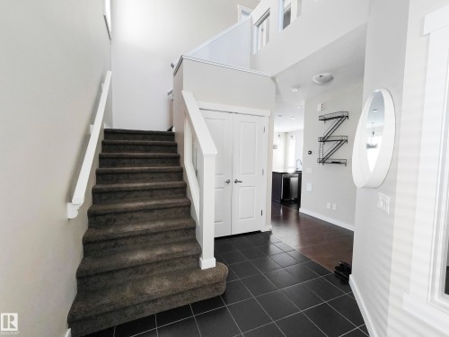 Entryway featuring dark tile flooring, a carpeted staircase with white railings, and a white coat closet - 8008 18 Avenue Sw, Edmonton, AB - Indoor Photo Showing Other Room
