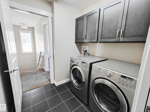 The laundry area features dark tiled flooring, dark upper cabinetry, and a light-colored wall - 8008 18 Avenue Sw, Edmonton, AB - Indoor Photo Showing Laundry Room