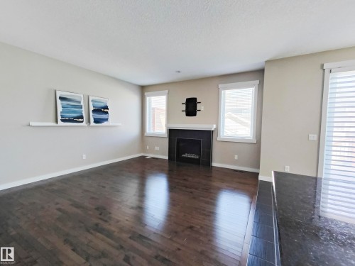 Living area featuring hardwood flooring, a fireplace with a dark surround, and white trim windows with blinds - 8008 18 Avenue Sw, Edmonton, AB - Indoor Photo Showing Living Room With Fireplace